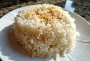 Close-up of a mound of fluffy Texas Roadhouse Seasoned Rice topped with melted butter and seasoning on a white plate.
