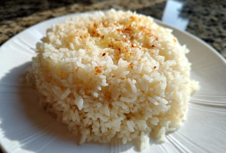Close-up of a mound of fluffy Texas Roadhouse Seasoned Rice topped with melted butter and seasoning on a white plate.