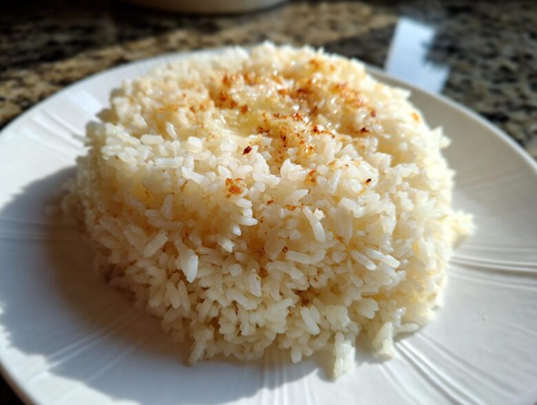 Close-up of a mound of fluffy Texas Roadhouse Seasoned Rice topped with melted butter and seasoning on a white plate.