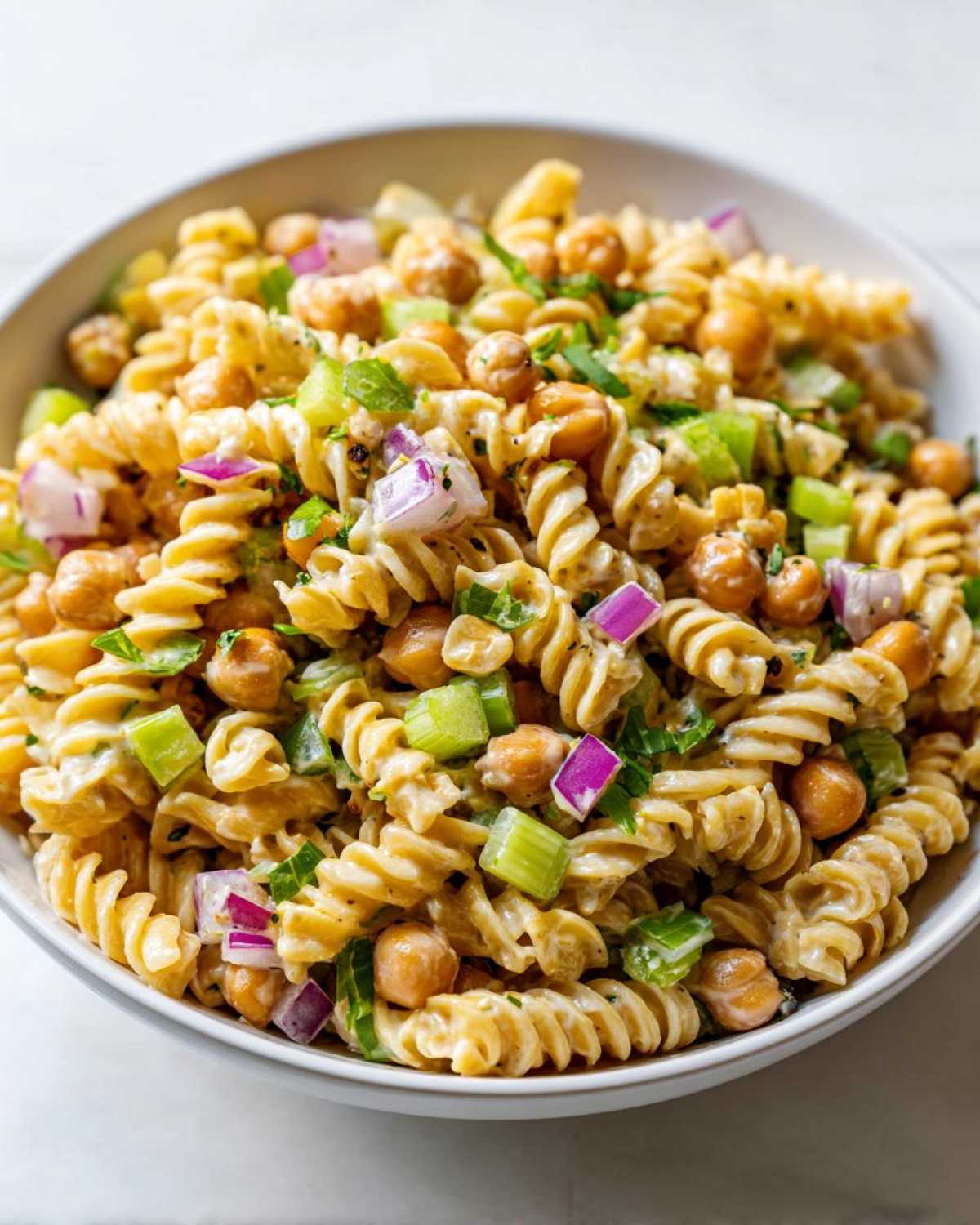 A close-up view of Vegan Creamy Lemon Chickpea Pasta Salad featuring fusilli pasta, chickpeas, celery, and red onion in a creamy dressing.