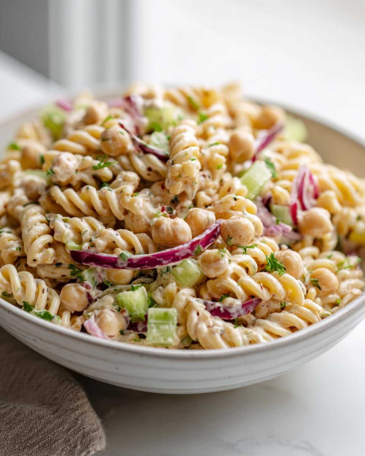 Close-up of Vegan Creamy Lemon Chickpea Pasta Salad featuring rotini pasta, chickpeas, red onion, and celery.