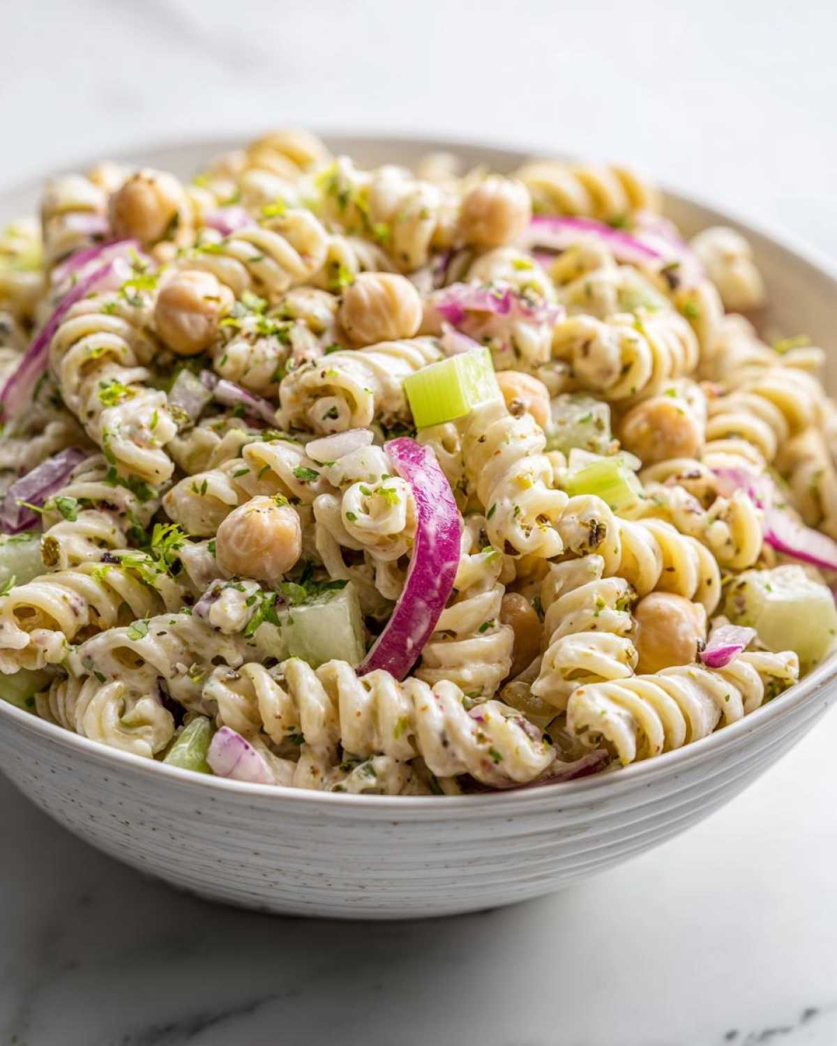 Close-up of Vegan Creamy Lemon Chickpea Pasta Salad featuring rotini pasta, chickpeas, red onion, and celery in a white bowl.