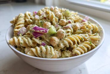 Close-up of a bowl filled with Vegan Creamy Lemon Chickpea Pasta Salad, featuring fusilli pasta, chickpeas, and red onion.