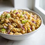 Close-up of Vegan Creamy Lemon Chickpea Pasta Salad featuring fusilli pasta, chickpeas, red onion, and celery in a white bowl.