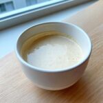A small white bowl filled with the creamy Vegan Creamy Lemon Tahini Dressing, resting on a light wooden surface.