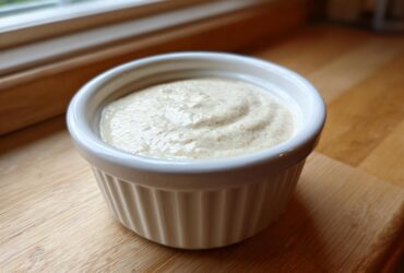 A close-up of thick Vegan Creamy Lemon Tahini Dressing swirled in a small white ceramic ramekin.