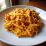 A close-up serving of pasta coated thickly in bright orange Vegan Creamy Sweet Potato Mac Sauce on a white plate.
