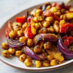 Close-up of roasted chickpeas, red onion wedges, and red bell peppers seasoned for Vegan One-Pan Chickpea Shawarma Sheet Bake.
