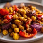 Close-up of roasted chickpeas, red bell peppers, and red onion wedges from the Vegan One-Pan Chickpea Shawarma Sheet Bake.