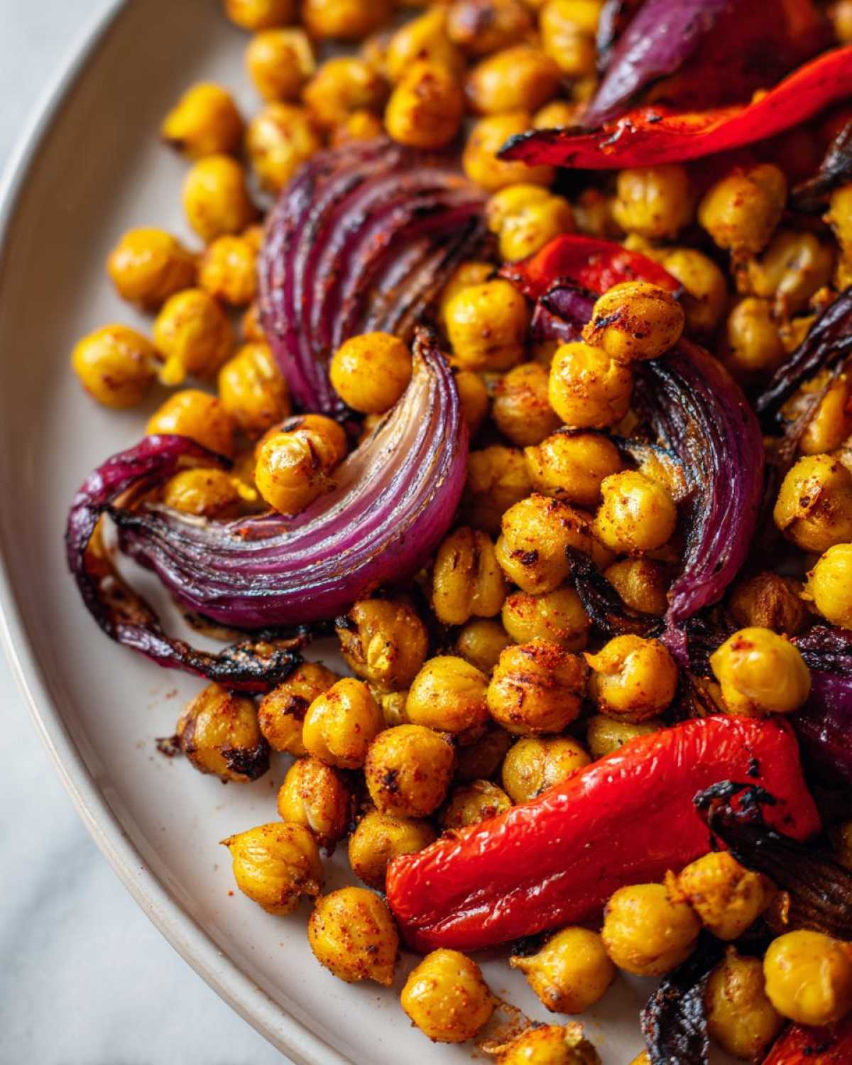 Close-up of roasted, spiced chickpeas mixed with wedges of red onion and strips of red pepper from the Vegan One-Pan Chickpea Shawarma Sheet Bake.