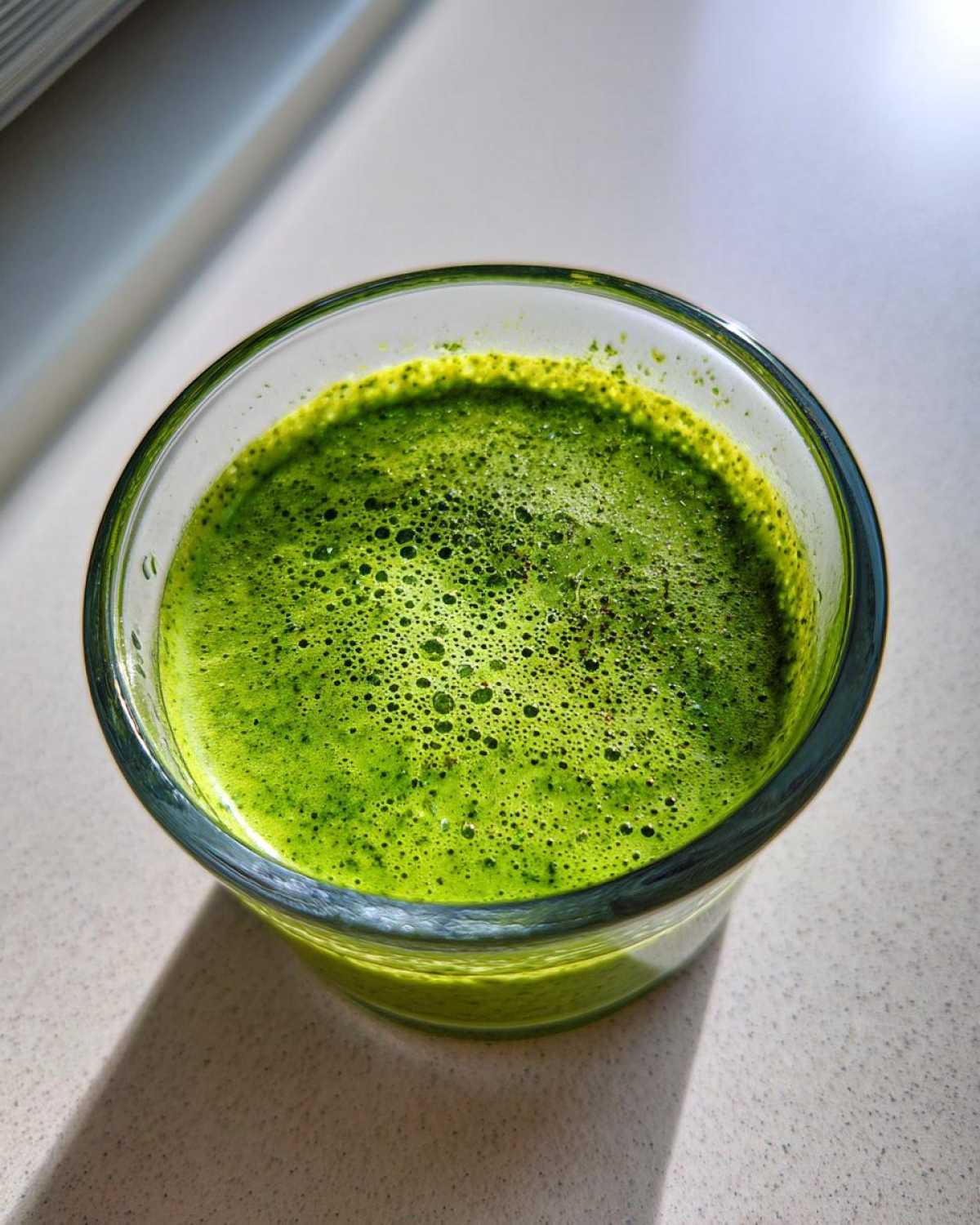 Close-up overhead shot of vibrant green Copycat Green Goddess Ranch Dressing with foam in a clear glass.